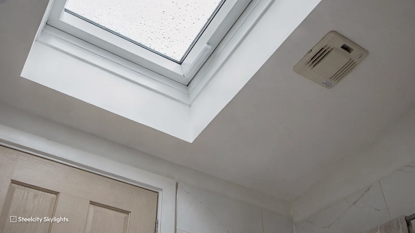 Roof window seen from inside with rain on the glass and a ventilation grille beside it