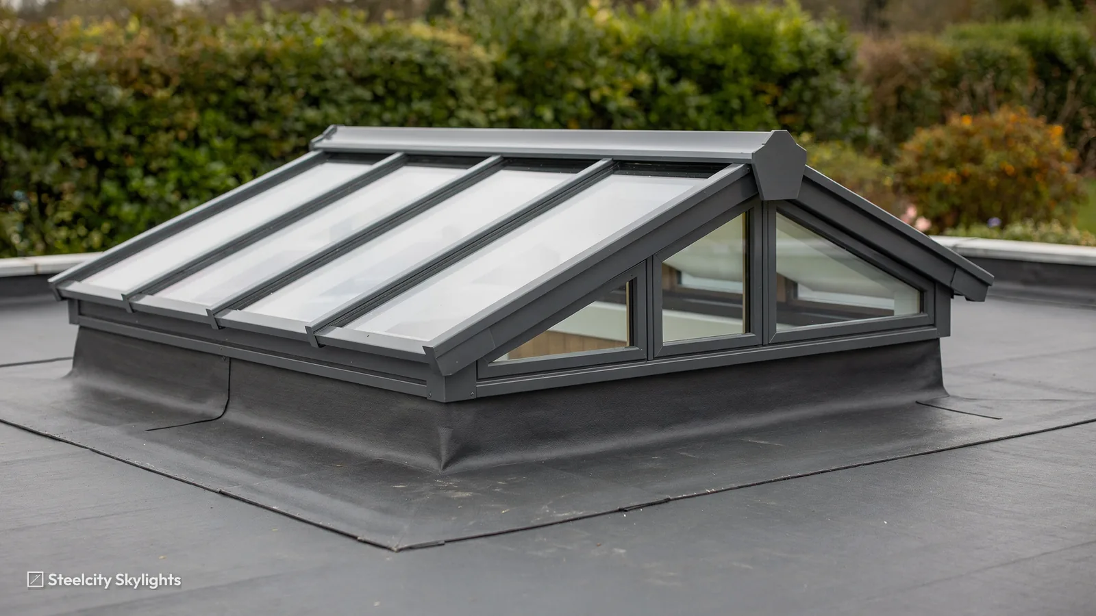 Grey aluminium roof lantern with a hipped end sitting on a single-ply flat roof