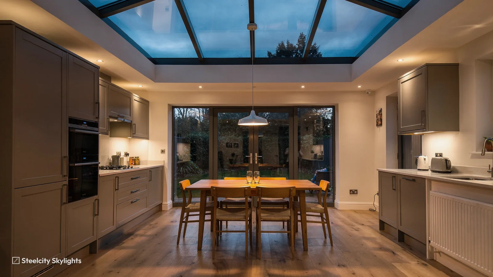 Kitchen-diner at dusk under a large rectangular roof lantern with sliding doors to the garden