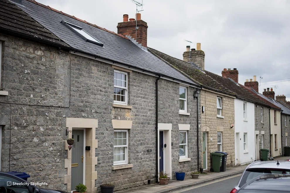 Row of grey stone terraced cottages on a street, with a roof window in the slate roof