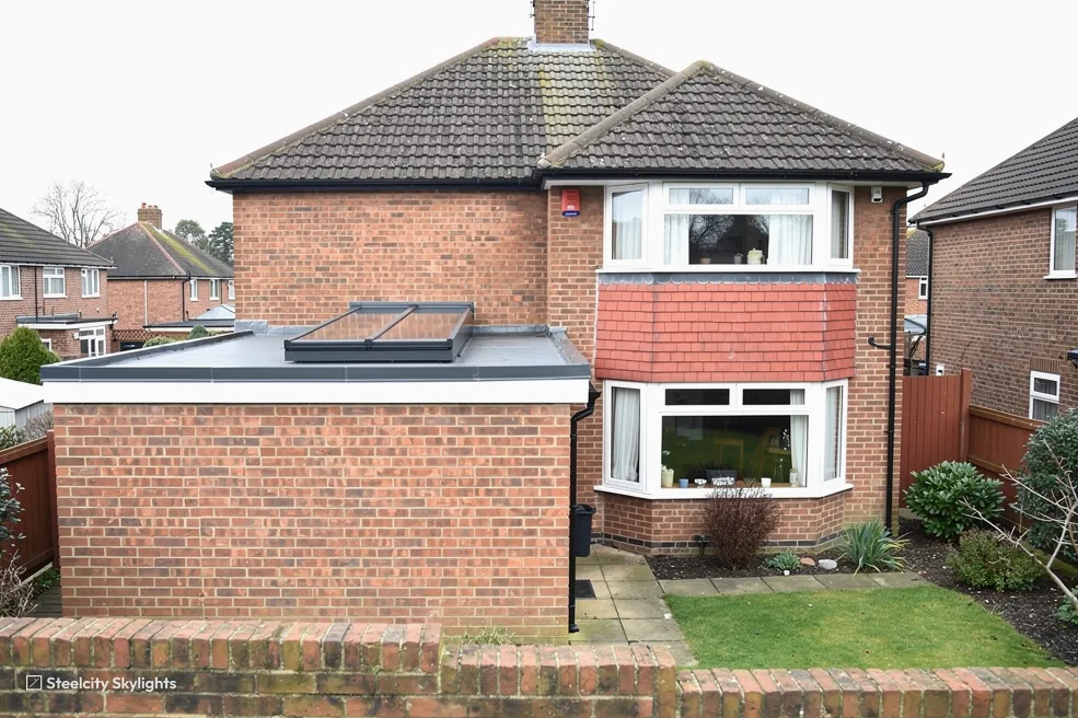 Brick semi with a single-storey flat-roofed extension and a flat rooflight, seen across the garden