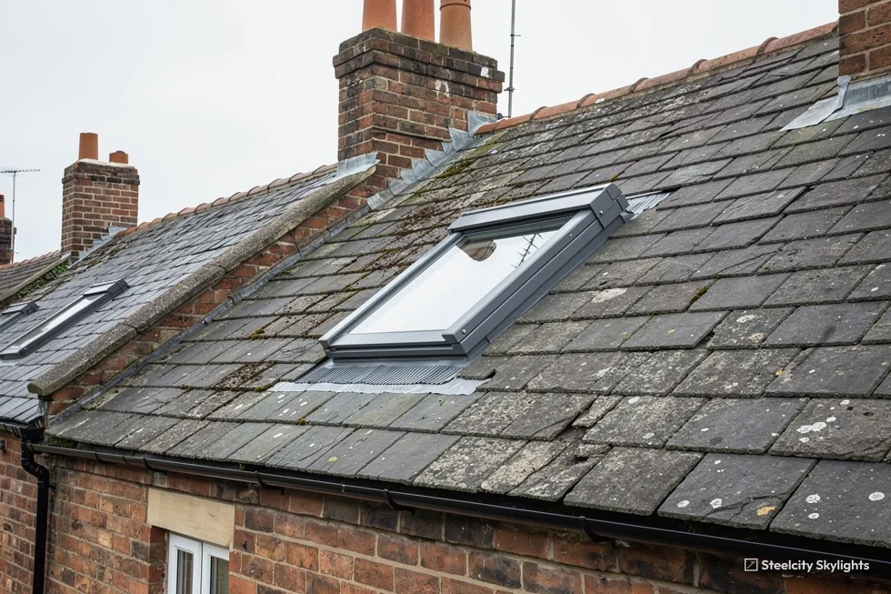 Roof window in a slate roof among brick chimneys on a row of terraced houses
