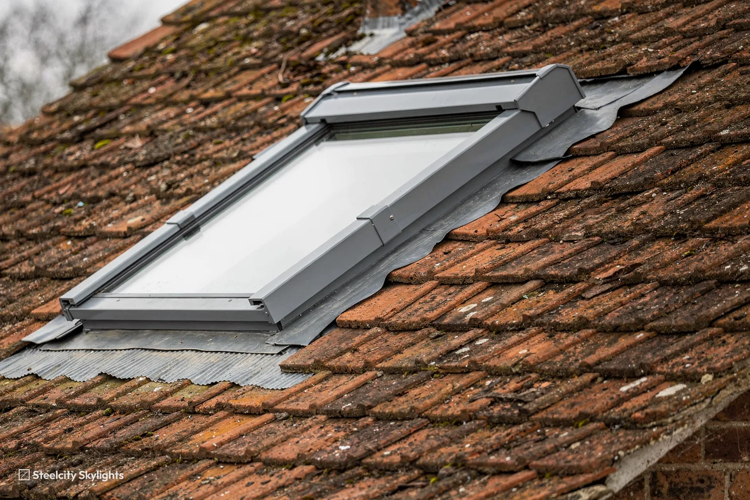 Newly flashed roof window with grey aluminium cladding in a red clay tile roof