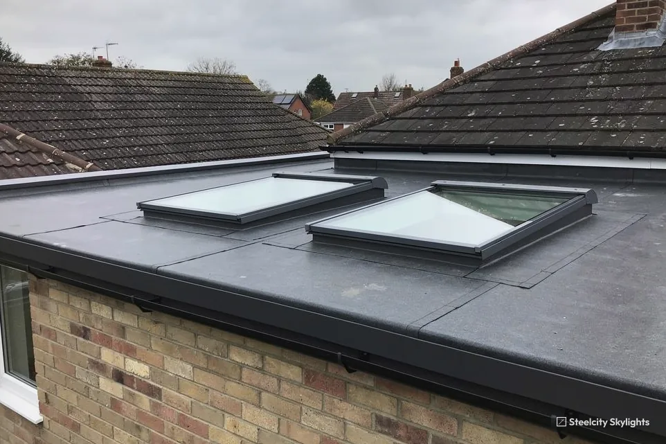 Two flat rooflights on the grey single-ply roof of a brick bungalow extension