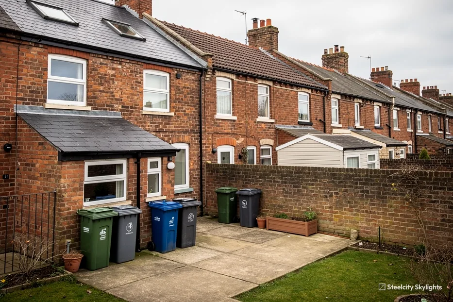Rear of a brick terrace with roof windows in the slate roofs, bins and a small yard