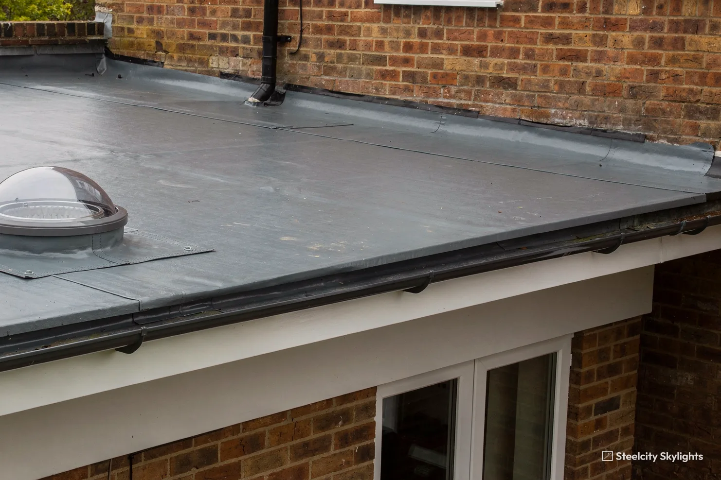 Clear domed sun tunnel cap on the grey flat roof of a single-storey extension