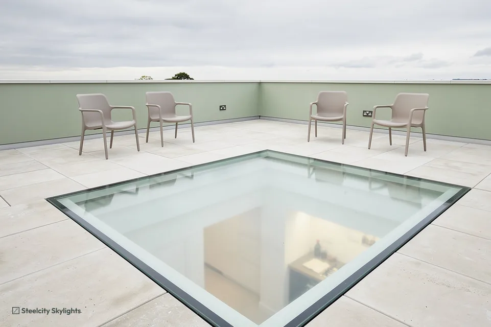 Walk-on glass panel in a pale paved roof terrace with four chairs and sage green walls