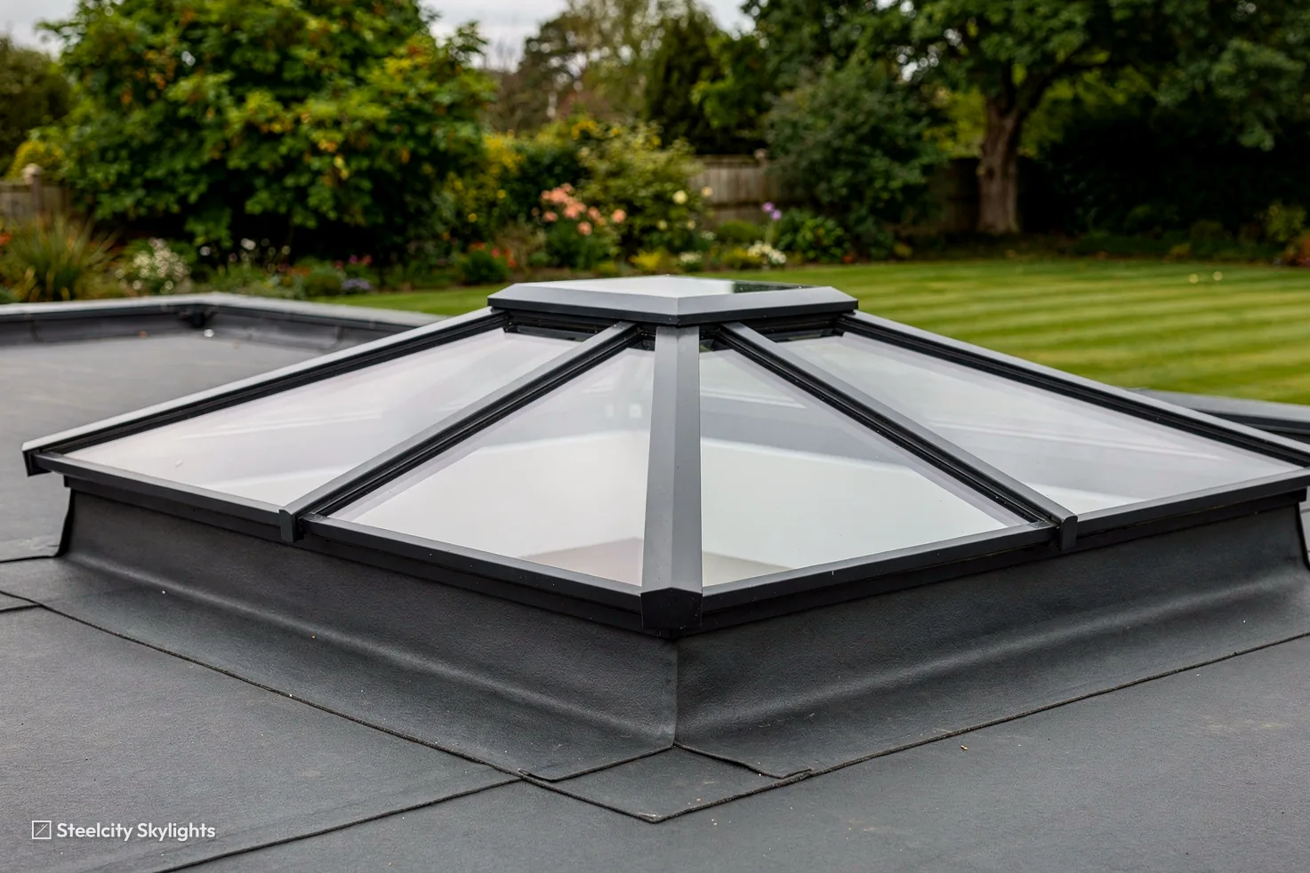 Hipped aluminium roof lantern with grey frames sitting on a flat roof above a striped lawn