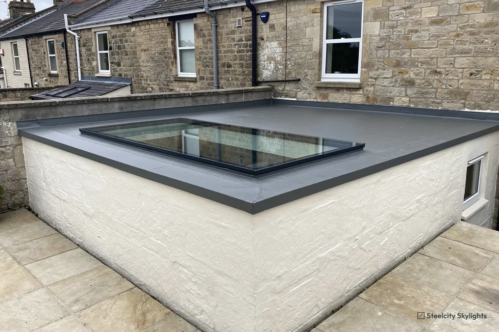 Painted brick single-storey extension with a flat rooflight, behind a stone terraced house