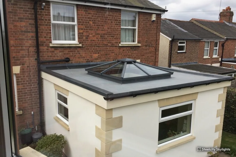 Small rendered extension with stone quoins and a pyramid roof lantern behind a brick house