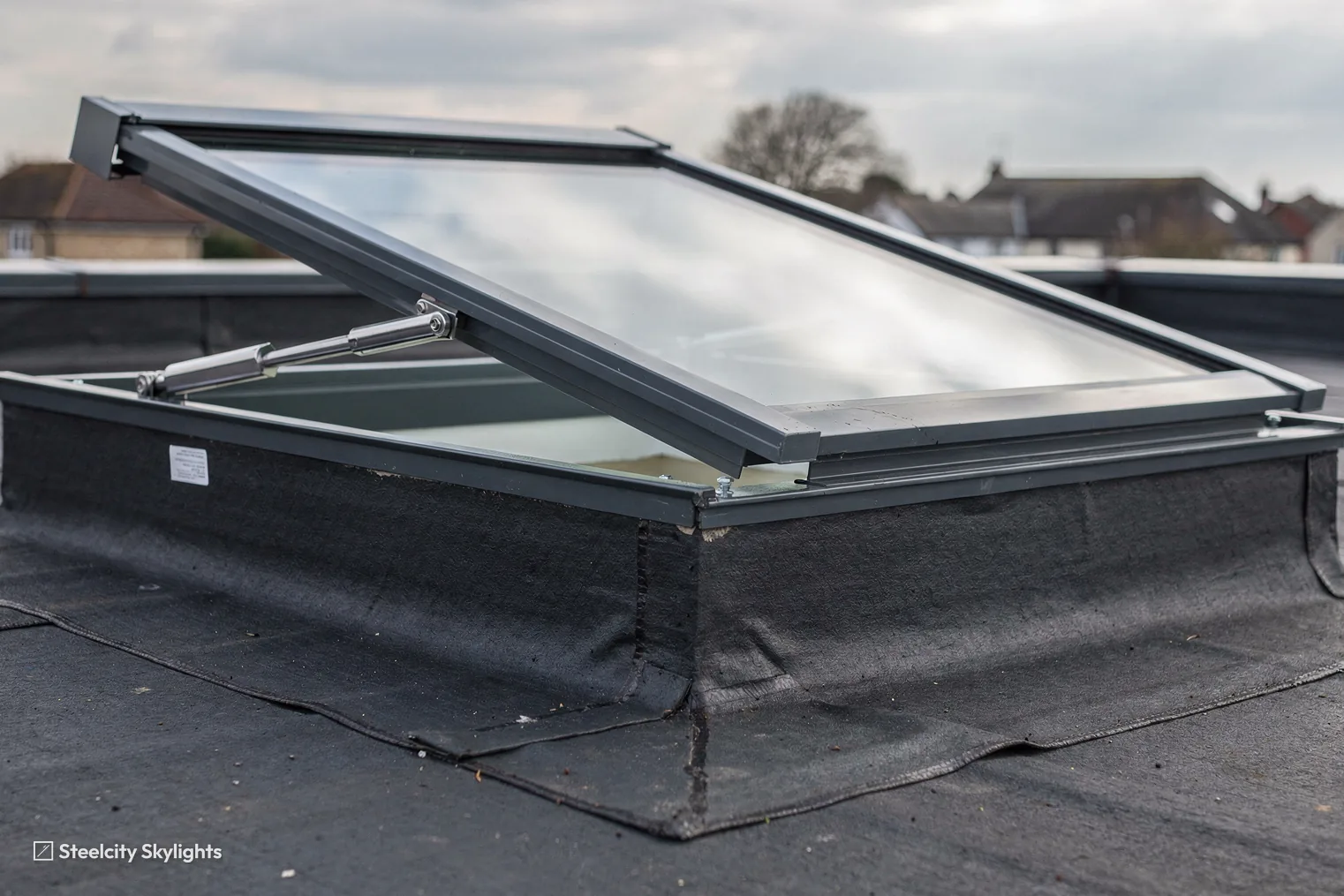 Close view of a hinged opening rooflight raised on its upstand on a flat roof