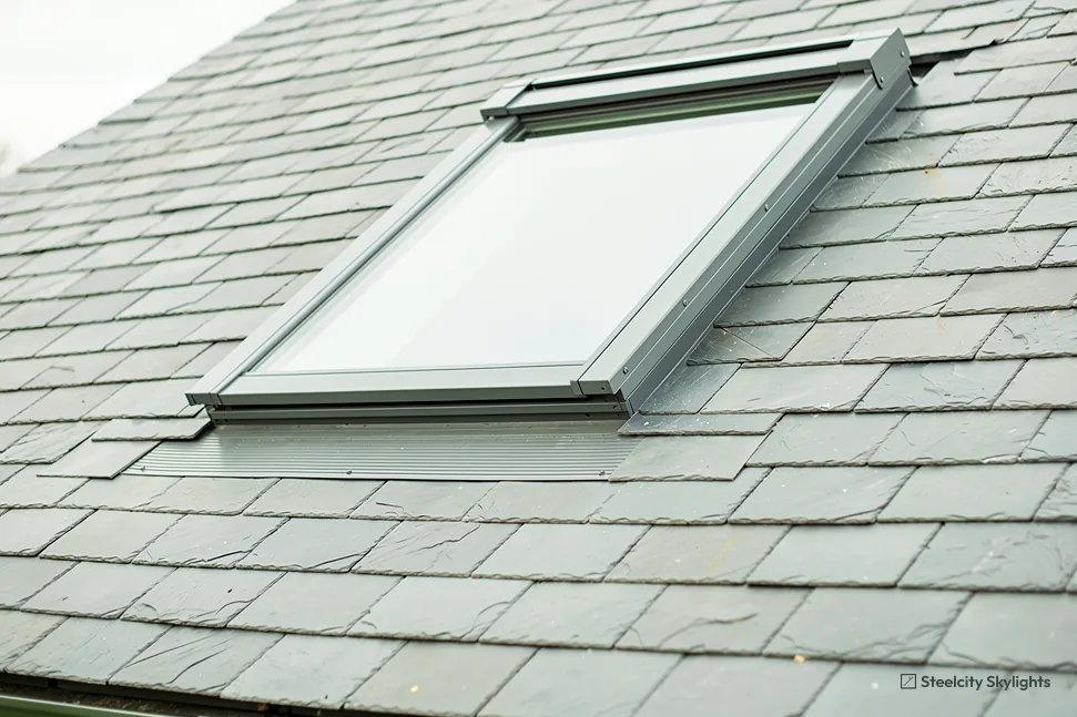 Roof window with grey flashing set into a pale green-grey slate roof