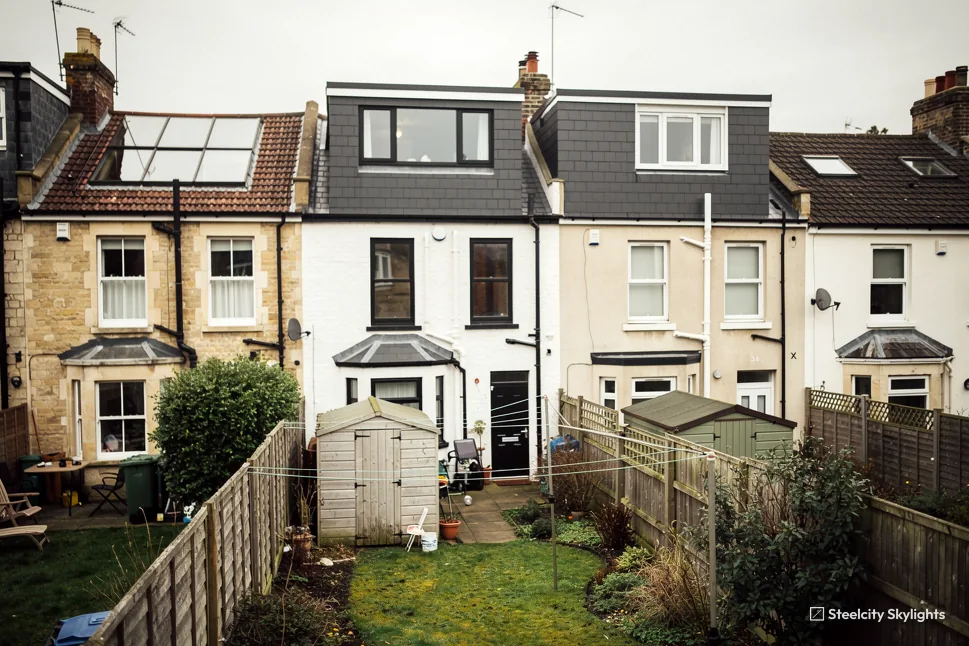 Rear of a row of terraced houses with dormer loft conversions, roof windows and long gardens